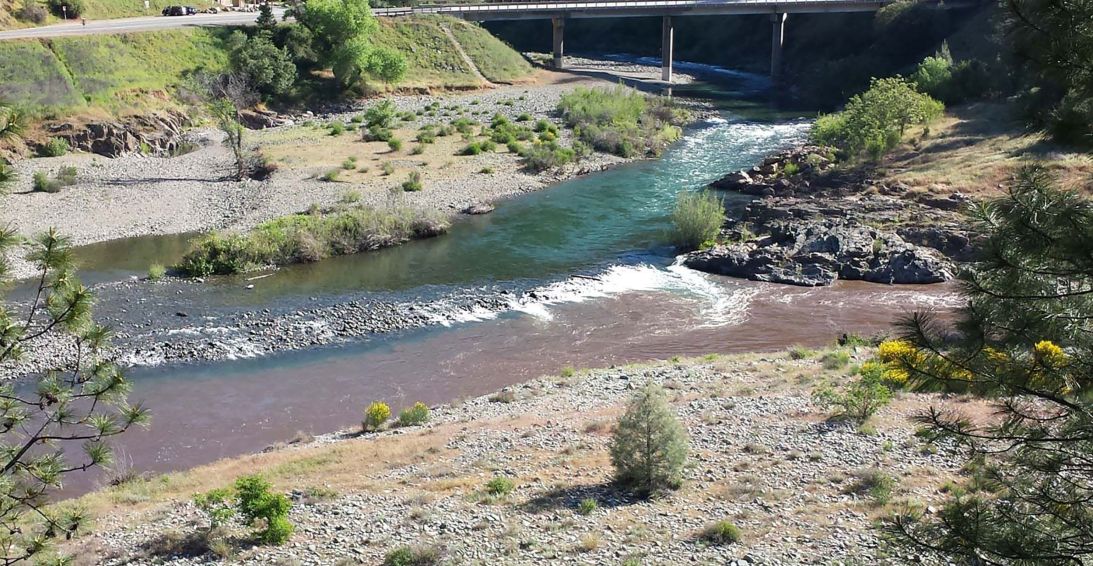 Brown sediment-filled runoff flowing into a clear river below a bridge